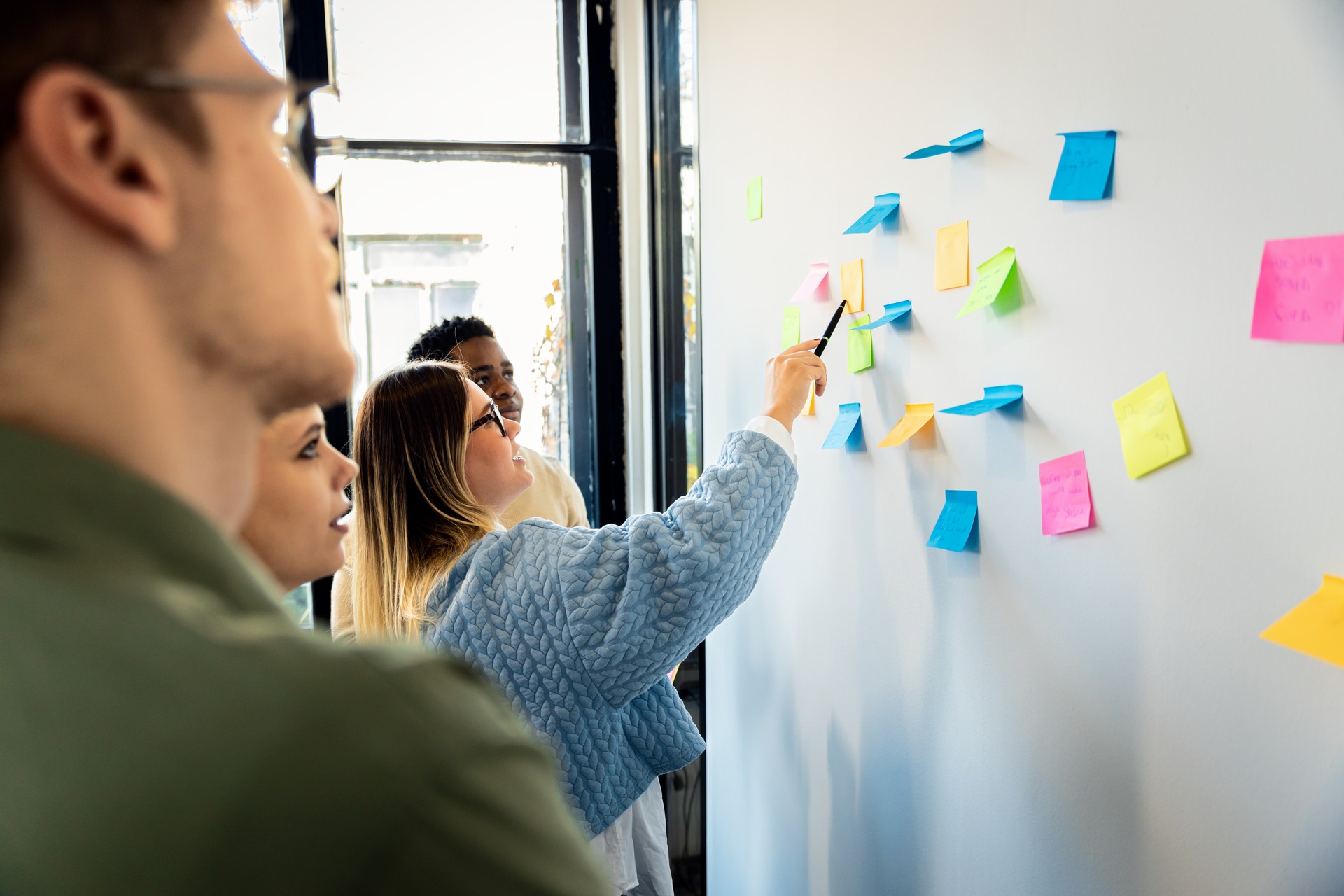 Diverse group of young business people working in office using colorful sticky notes on wall to organize their ideas.